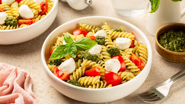 A bowl of pasta salad with cheese, pesto, and tomatoes