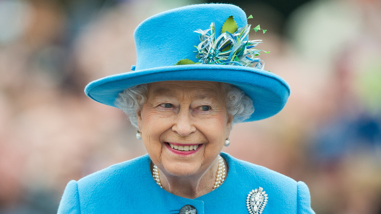 Smiling Queen Elizabeth II, from shoulders up, wearing a blue suit and hat