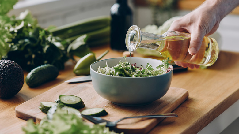 White wine vinegar being poured over a bowl of salad greens