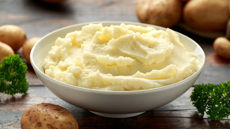 bowl of mashed potatoes surrounded by whole potatoes 
