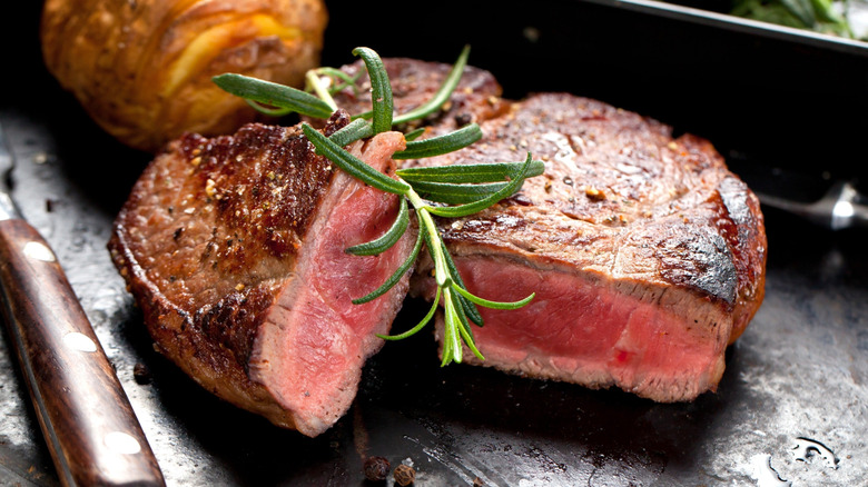 Cooked steak on griddle cut in half and garnished with rosemary sprig