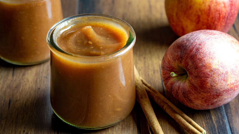 Jar of homemade apple butter surrounded by fresh apples