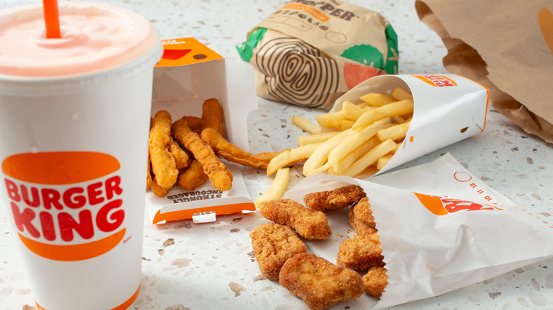 A Burger King Whopper, fries, and nuggets, sitting on a table with a Burger King bag