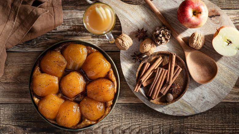 An apple tart and apple cider next to cinnamon sticks