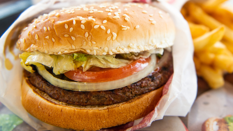 Burger King Whopper in wrapper beside fries on table