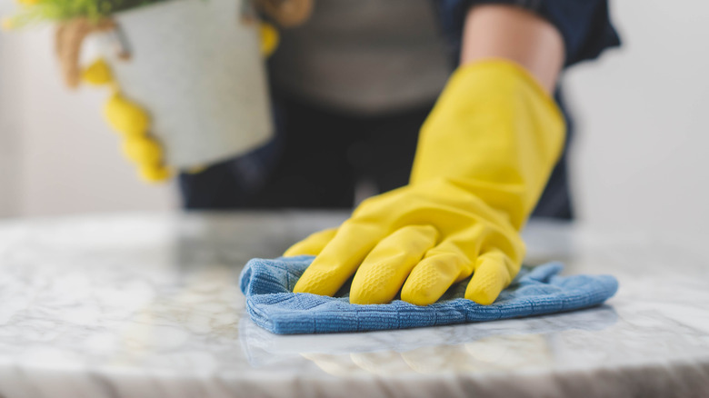 Person wearing yellow gloves wiping blue cloth over gray marble table