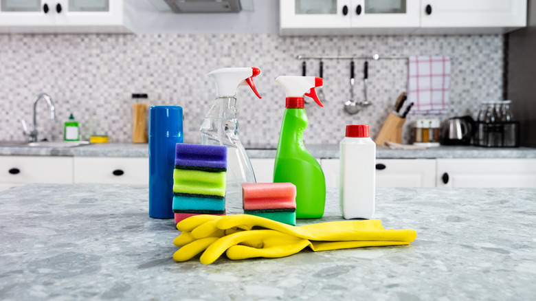 Pale gray marble countertop with cleaning products including gloves, sponges, and spray bottles on surface