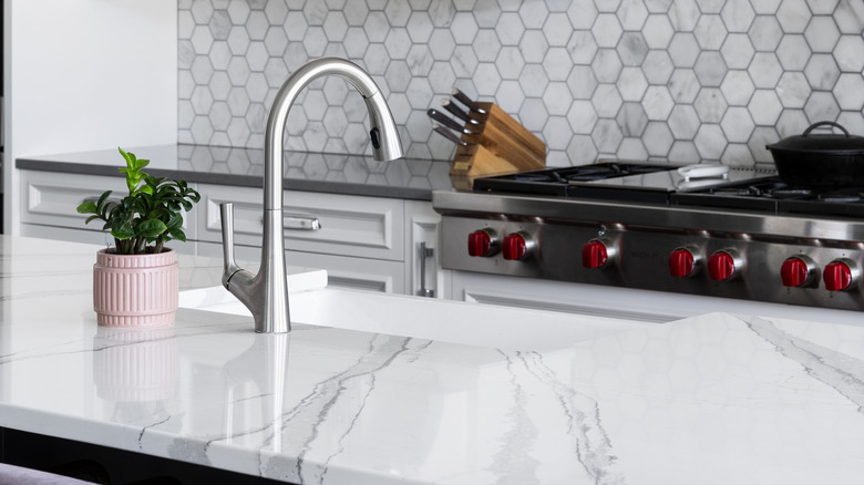 Kitchen with white marble counter, white cabinets, and tiled gray backsplash