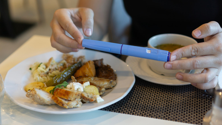 A diner holding a GLP-1 injection pen over a plate of food in a restaurant.