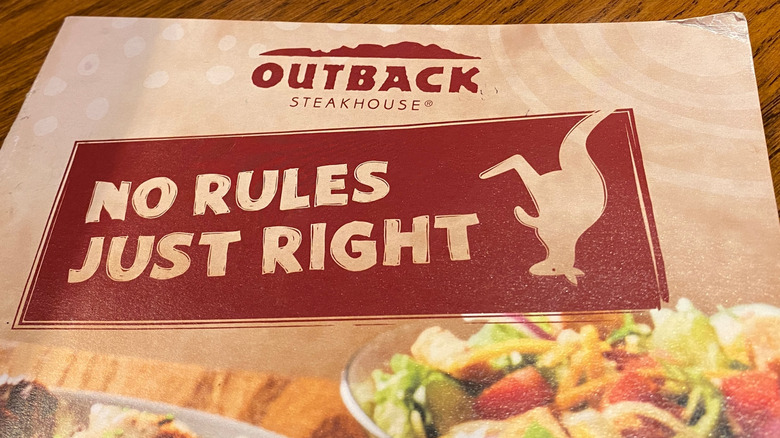 An Outback Steakhouse menu sitting on a table featuring an upside down kangaroo logo and an image of a salad