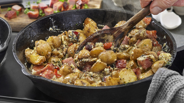 Stirring a cast iron skillet of breakfast hash with a wooden spoon