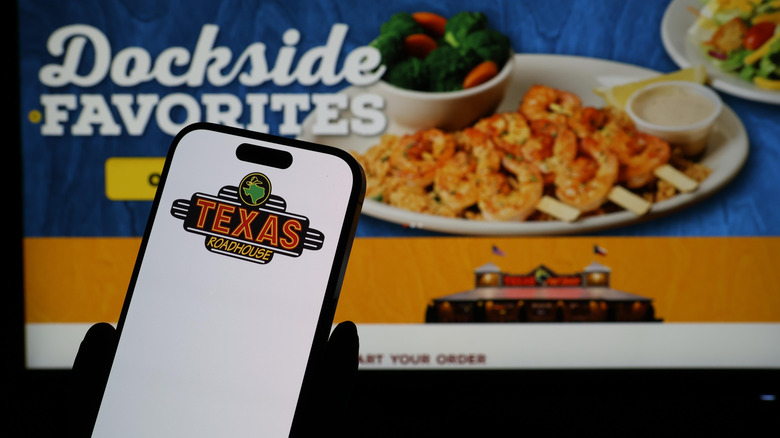 Smartphone with Texas Roadhouse logo in front of web page with shrimp dish