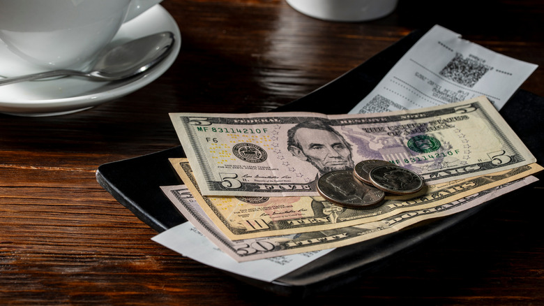Bills, change, and reciept on black tray on restaurant table