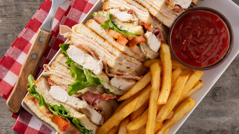 Club sandwich with fries on white plate