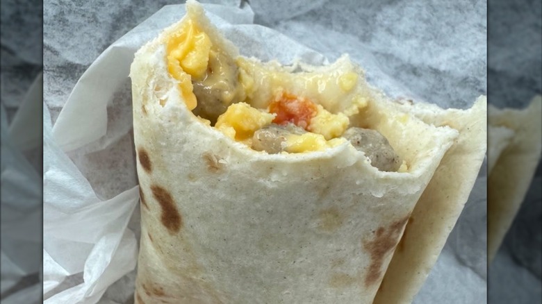 A McDonald's Sausage Burrito with a couple of bites out of it showing the egg, sausage, and veggies inside
