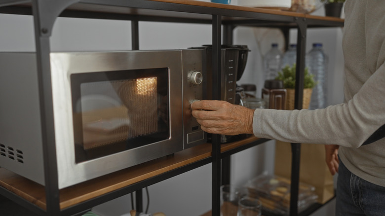 A hand turning the knob on a microwave that sits on one segment of a large open storage shelf