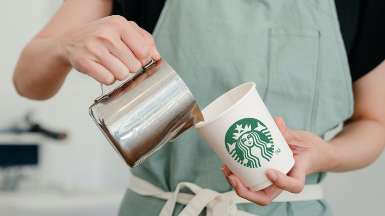 barista pouring hot milk into Starbucks cup