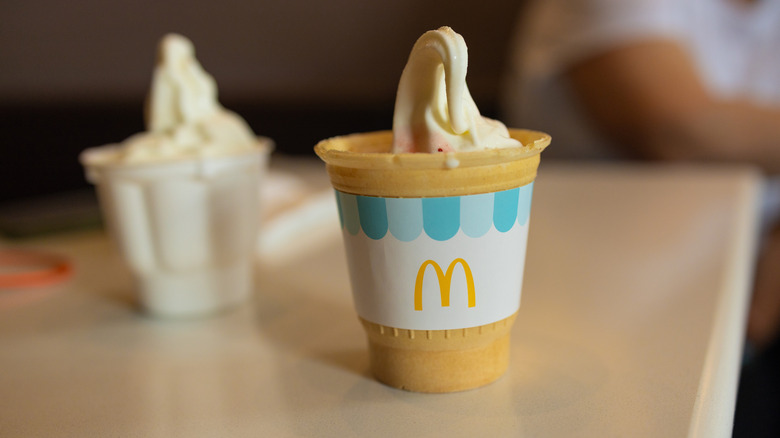 Two cups of McDonald's vanilla ice cream in cups on a counter, the one in the foreground is in a tan recyclable cup
