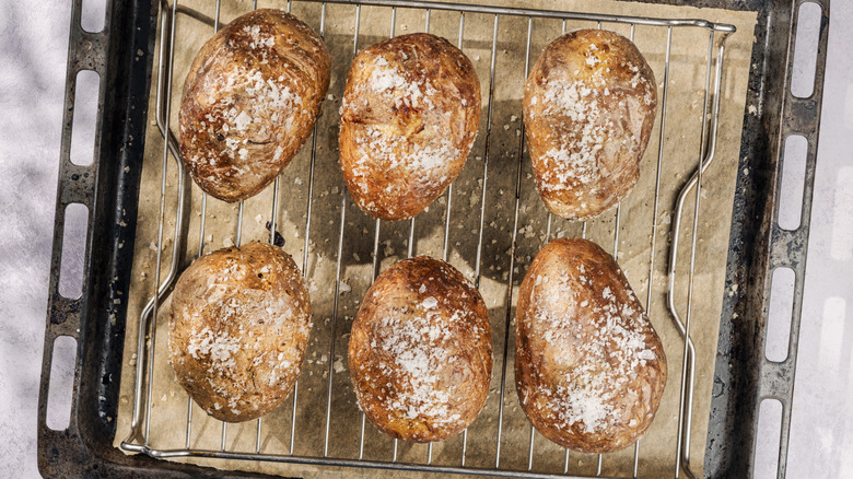 Baked potatoes on a wire rack over a baking sheet, finished with sea salt