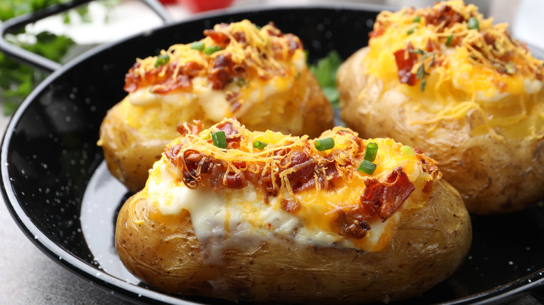 Three baked potatoes with sour cream, cheese, and bacon bits on a black plate