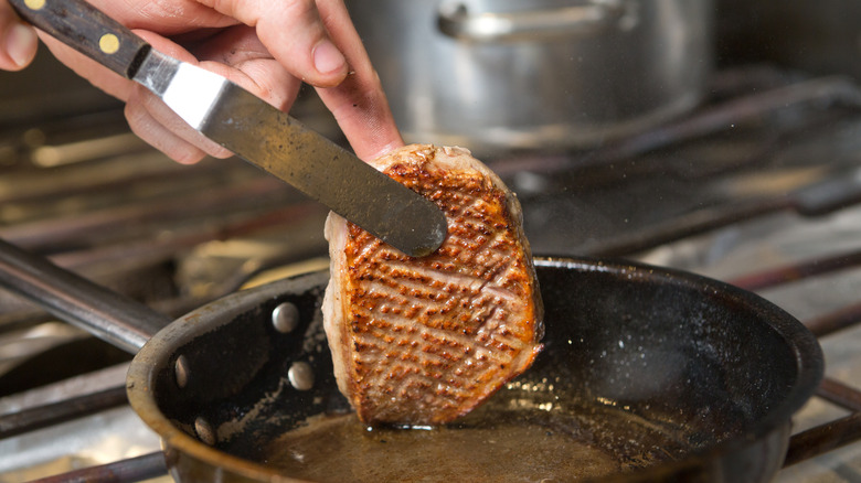 Lifting duck breast from frying pan to show crispy skin