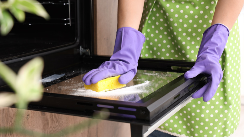 Hands in gloves cleaning oven door