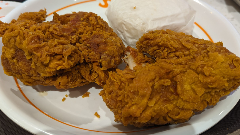 Two pieces of Popeye's fried chicken and a wrapped biscuit on a paper plate