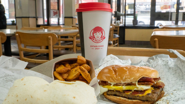 A Wendy's Baconator meal deal with a cup of coffee, the baconator sandwich, and a side of the seasoned potato wedges with an add on breakfast burrito