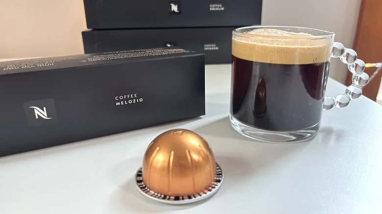 A Melozio coffee pod in front of a brewed mug and a sleeve of the pods