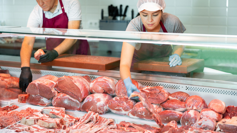 Two butchers putting beef into a full display case with different cuts