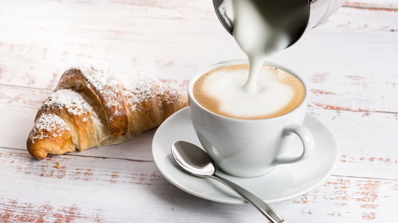 milk frother pouring into mug with croissant