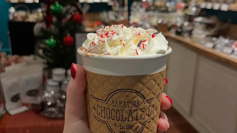 A woman's hand holding a cup with Saratoga Chocolate Co on it