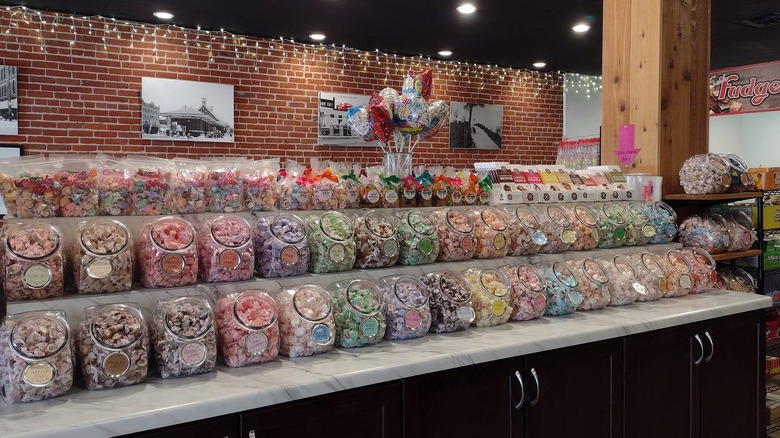 Variety of candy in jars on a shelf with a facebrick wall behind
