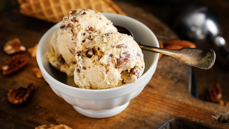 Scoops of butter pecan ice cream in white bowl with spoon