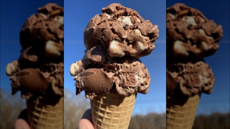 Hand holding waffle cone with two scoops of rocky road ice cream