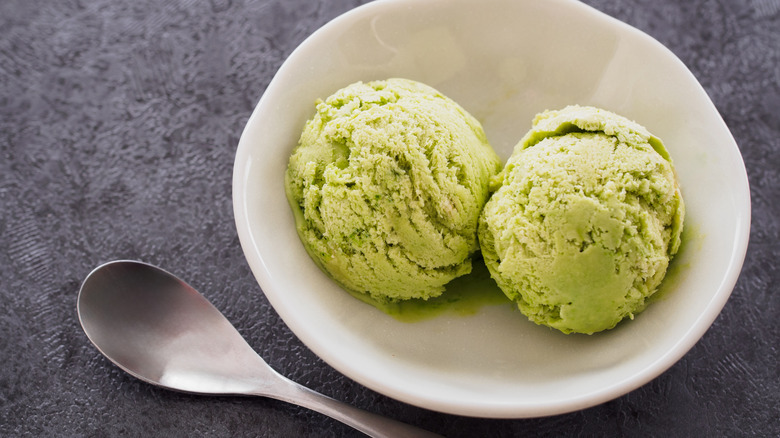 Two scoops of matcha ice cream in white bowl with spoon