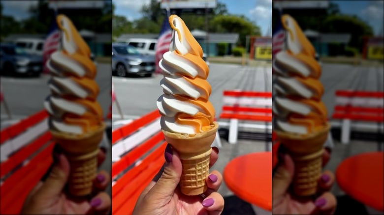 Hand holding cone of orange swirl ice cream