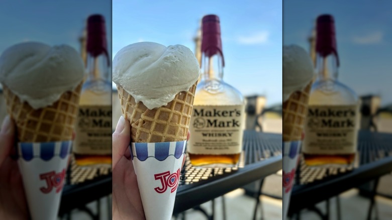 Hand holding vanilla ice cream cone with bottle of whisky in background