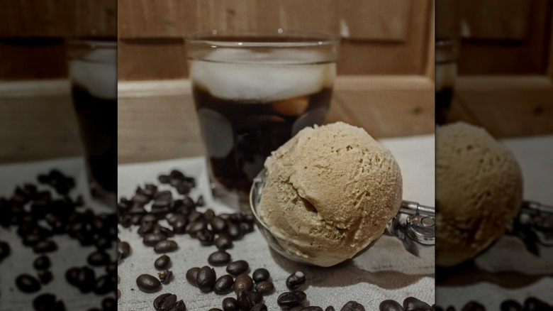 Scoop of coffee ice cream next to glass of brewed coffee and dried coffee beans