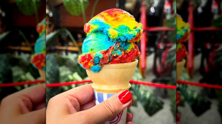Hand holding cone filled with rainbow-colored ice cream