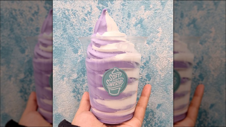 Hand holding tub of Soft Swerve ube and coconut ice cream