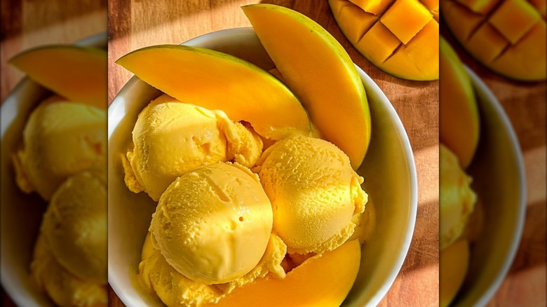 Scoops on mango ice cream in bowl with fresh mango wedges