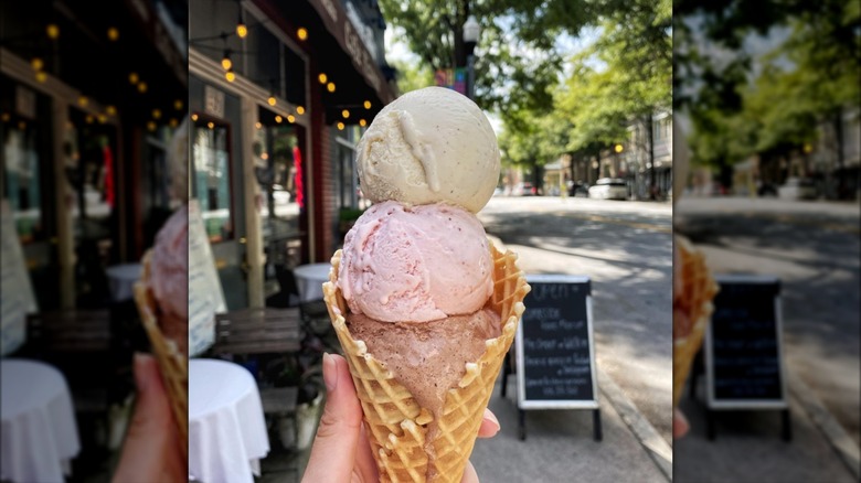 Hand holding cone filled with scoops of vanilla, chocolate, and strawberry ice cream