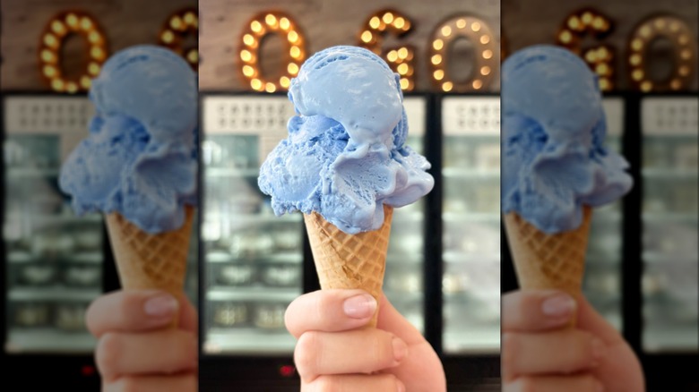Hand holding cone filled with blue cotton candy ice cream