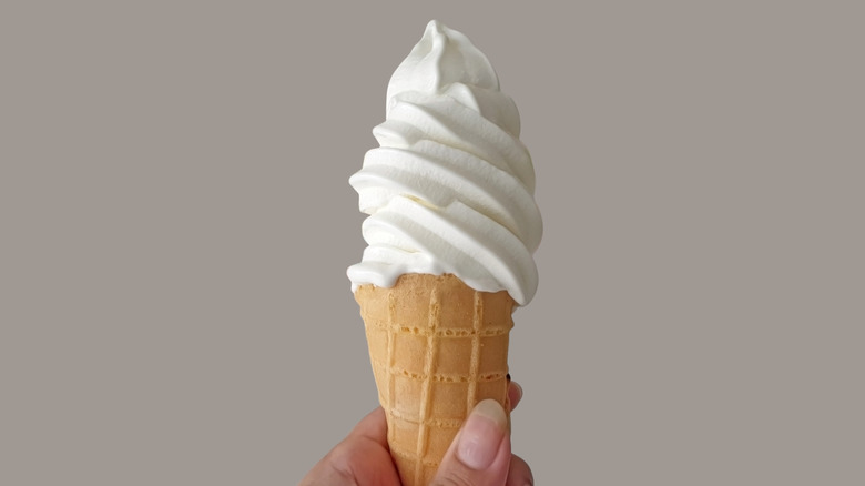 Hand holding soft serve vanilla ice cream cone