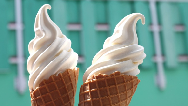 Two vanilla soft serve ice cream cones against backdrop of teal building
