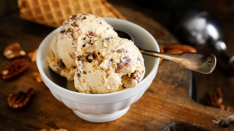 Two scoops of butter pecan ice cream inside white dish with spoon