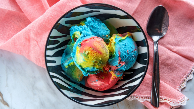 Scoops of colorful Superman ice cream in zebra printed bowl next to spoon on pink cloth