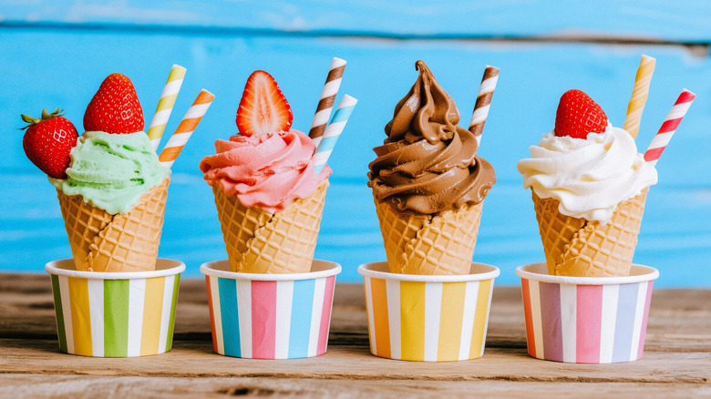 Ice creams cones including mint, chocolate, strawberry, and vanilla flavors inside colorful striped paper cups with strawberries and colorful striped straws