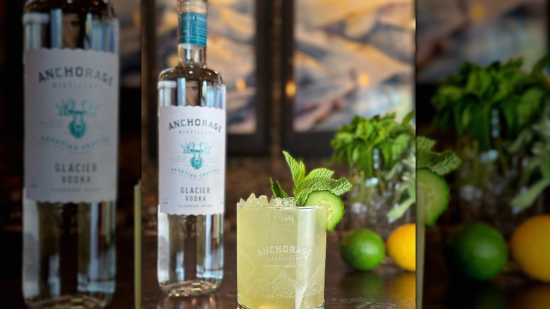 A bottle of Anchorage vodka next to a cocktail with mint and cucumber garnish.